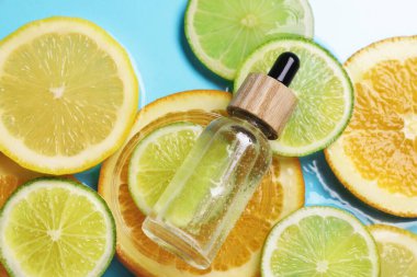 Bir şişe cilt bakımı ürünü ve narenciye açık mavi arka planda suda doğranır.