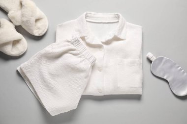 Modaya uygun beyaz pijamalar, uyku maskesi ve açık gri arka planda terlikler, düz yatış.