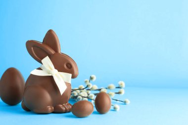 Çikolatalı Paskalya tavşanı, yumurtalar ve açık mavi arka planda söğüt dalları. Metin için boşluk
