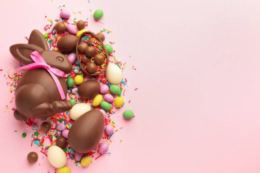 Çikolatalı Paskalya tavşanı, yumurtalar, şekerler ve pembe arka plana serpiştirilmiş şekerler, düz yatak. Metin için boşluk