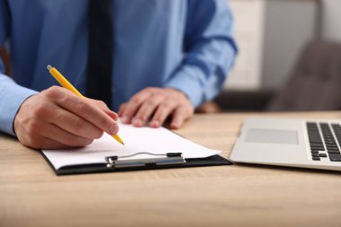 İçerideki ahşap masada kalemle panoya yazı yazan adam, yakın plan.