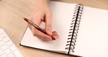 Ahşap masada kalemle deftere yazan kadın, yakın plan.