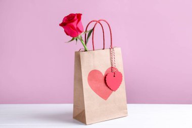 Kalpli hediye çantası ve pembe arka planda beyaz masada gül. Sevgililer Günü