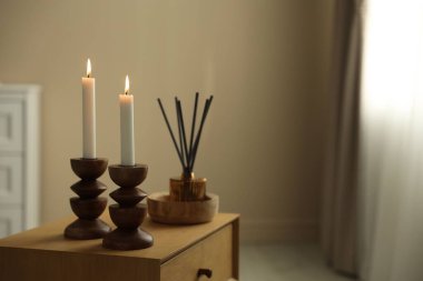 Zarif şamdanlar, yanan mumlar ve ahşap şifoniyer üzerinde sazlık dağıtıcı.