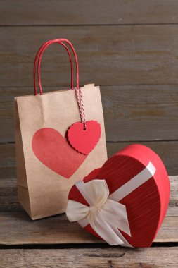 Kağıt torba ve kalp şeklinde hediye paketi ahşap masada.