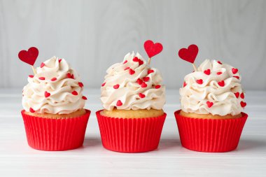 Sevgililer Günün kutlu olsun. Gri duvarın yakınındaki beyaz ahşap masada kalpler şeklinde serpiştirilmiş lezzetli kekler, yakın plan.