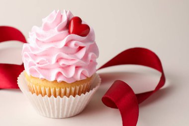 Sevgililer Günün kutlu olsun. Dekoratif kalbi olan lezzetli kek ve açık gri arka planda kırmızı kurdele, yakın plan.