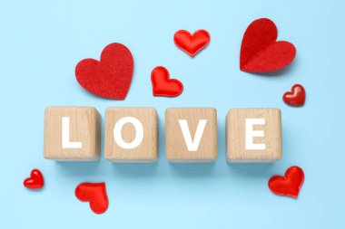 Aşk sözcüğüyle ahşap küpler ve açık mavi arka planda kırmızı kalpler, düz yatış. Tebrik kartı