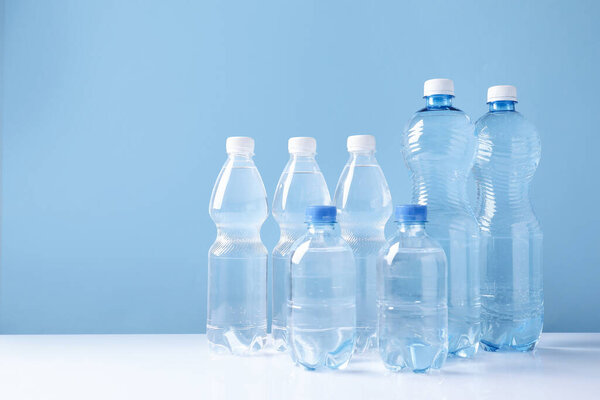 Water bottles of different sizes on white table against light blue background. Space for text
