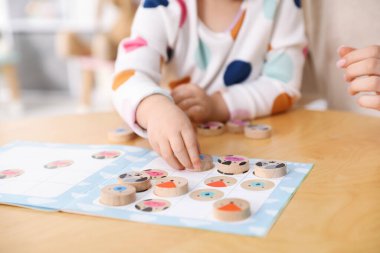 Anne ve kızı içeride ahşap masada oyuncaklarla oynuyor, yakın plan.