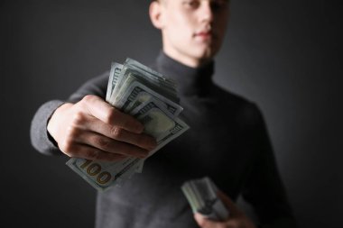 Genç işadamı karanlık arka planda dolar banknotları veriyor, yakın plan