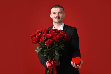 Sevgililer Günü kutlaması. Güzel gül buketi ve kırmızı arka planda kalp şeklinde kutusu olan bir adam.