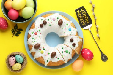 Lezzetli Paskalya pastası, boyanmış yumurtalar, söğüt dalı, sunucu ve yeşil yapraklar sarı arka planda, düz uzanmış