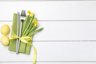 Paskalya sofrası. Nergisli güzel gümüş takımlar ve beyaz ahşap arka planda boyanmış yumurtalar, üst manzara. Metin için boşluk