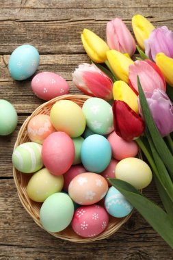 Hasır sepetin içinde boyanmış Paskalya yumurtaları ve ahşap masanın üzerinde güzel laleler.