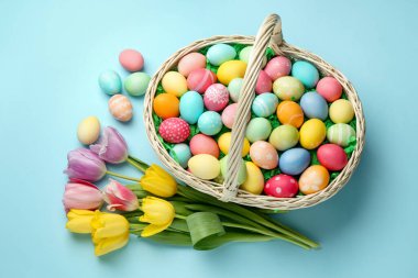 Açık mavi zemin üzerinde boyanmış yumurtalar ve laleler olan Paskalya sepeti düz yatıyordu.