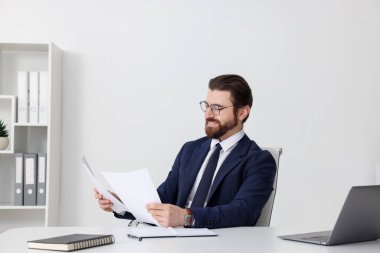 Beyaz duvarın yanındaki masada çalışan bir iş adamı.