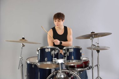 Çubuklu genç çocuk gri arka planda davul çalmayı öğreniyor.