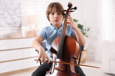 Evdeki sandalyede keman çalan küçük çocuk.