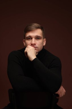 Moda modeli. Koyu kahverengi arka planda poz veren yakışıklı bir adamın portresi.