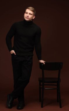 Moda modeli. Koyu kahverengi arka planda sandalyeli yakışıklı bir adam.