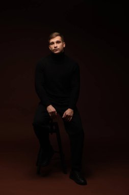 Moda modeli. Koyu kahverengi arka planda poz veren yakışıklı bir adam.