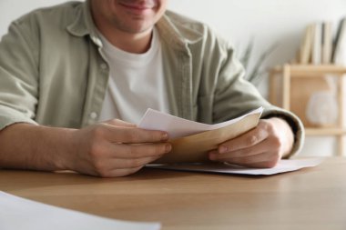 İçerideki ahşap masada mektupla zarfı açan adam, yakın plan.
