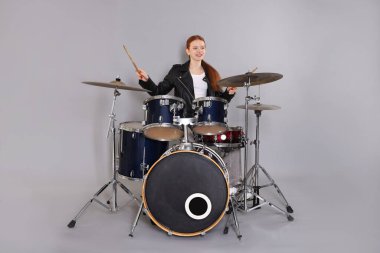 Açık gri arka planda bagetleri ve davulları olan genç bir kız.