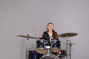 Açık gri arka planda bagetleri ve davulları olan genç bir kız.