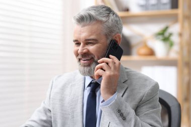 Ofiste akıllı telefonla konuşan takım elbiseli güler yüzlü bir işadamı.