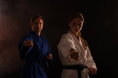 Üniformalı kadın ve erkek siyah arka planda dumanlı karate yapıyor.
