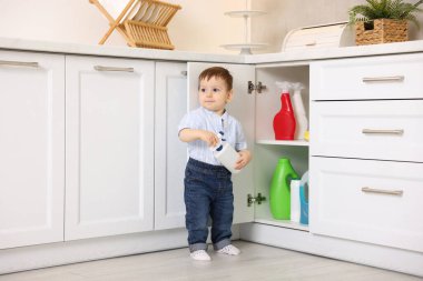 Evde çocuk güvenliği. Küçük çocuk mutfakta temizlik ürünleriyle dolap açıyor.