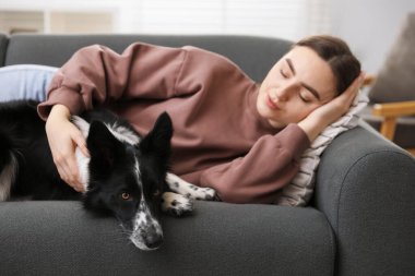 Evdeki kanepede uyuyan sevimli köpeğiyle genç bir kadın.