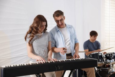 Gençlik bandosu içeride müzik öğretmeniyle performans çalışması yapıyor.