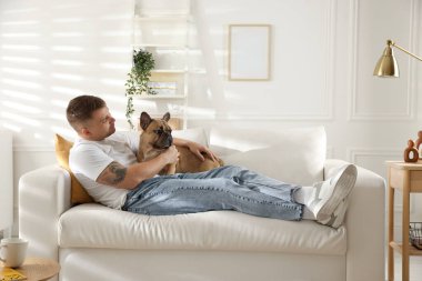 Evdeki kanepede dinlenen sevimli köpeğiyle genç bir adam.