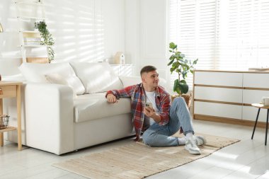 Akıllı telefonlu genç adam evde kanepenin yanında dinleniyor.