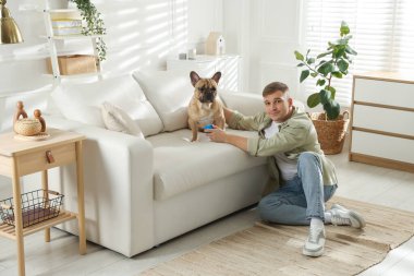 Evdeki kanepenin yanında sevimli köpeği ve oyuncağıyla genç bir adam.