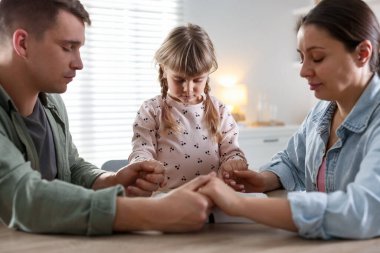 İncil 'i olan bir aile ahşap masada birlikte dua ediyor.
