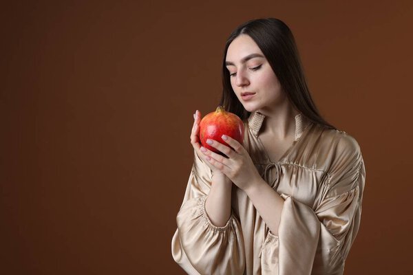 Beautiful woman with ripe pomegranate on brown background. Space for text