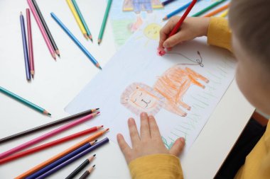 Küçük çocuk masada kalemle aslan çiziyor, yakın plan.