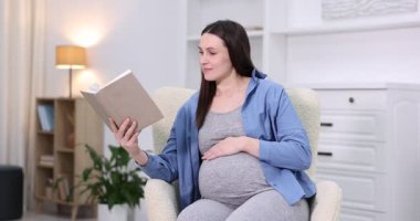 Hamile kadın evdeki koltukta kitap okuyor.