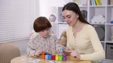 Anne ve oğlu içeride tahta masada oyuncaklarla oynuyorlar.