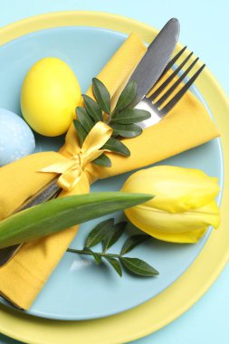 Paskalya kutlaması. Lale çiçeği, yeşil yapraklar ve açık mavi arka planda boyanmış yumurtalar, üst manzara.