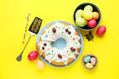 Lezzetli Paskalya pastası, boyanmış yumurtalar, söğüt dalı, sunucu ve yeşil yapraklar sarı arka planda, düz uzanmış