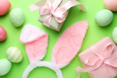 Boyalı Paskalya yumurtaları, tavşan kulaklıkları ve yeşil arka planda hediyeler, düz yatış.