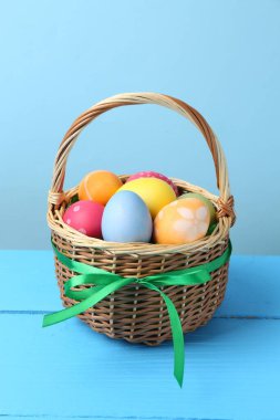 Hasır sepetin içine boyanmış Paskalya yumurtaları açık mavi arka plana karşı ahşap masada.