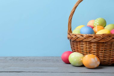 Hasır sepetin içine boyanmış Paskalya yumurtaları açık mavi arka planda gri ahşap masa üzerinde. Metin için boşluk