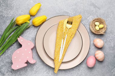 Paskalya kutlaması. Lale çiçekleri, çatal bıçak takımı ve gri desenli masa üzerine boyanmış yumurtalarla süslü bir yer.