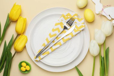 Paskalya kutlaması. Renkli yumurtalar, lale çiçekleri ve bej arka planda çatal bıçak seti olan şenlik masası.