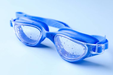 Açık mavi arkaplanda su damlaları olan yüzme gözlükleri, yakın plan